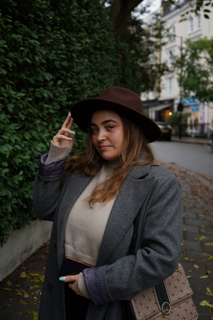 Portrait of a woman in a brown hat beside an ivy wall