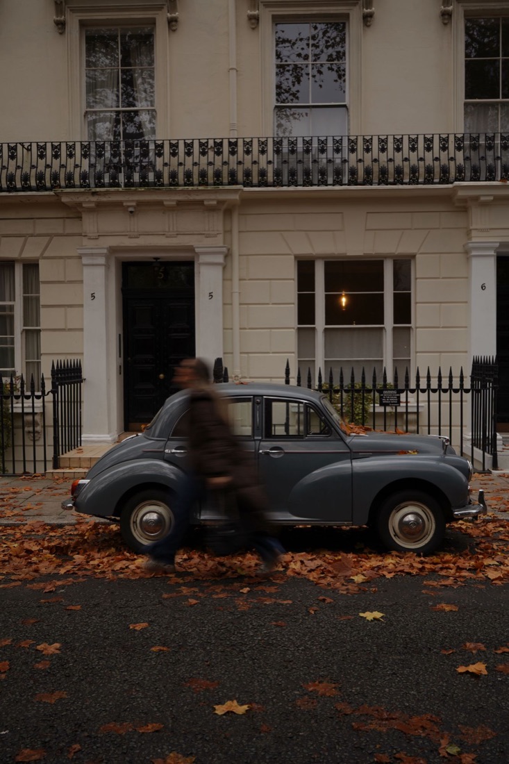 Classic grey car on autumn leaves with a blurred passer-by