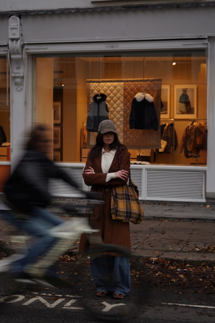Woman standing in front of a shop window as a cyclist blurs past